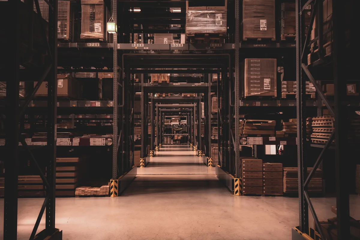 Warehouse aisle between tall storage racks filled with boxed goods.